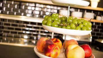 Een drijvende kraam vol fruit: groene druiven op het bovenste niveau, perziken in het midden, en een wit bord met perziken onderaan.