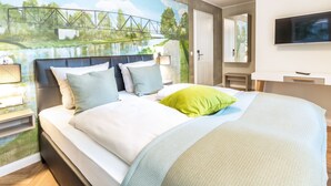 A modern bedroom with a bed, a nightstand, a TV, and a mural of a bridge. - Burghotel Lingen (Lingen)