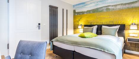A bedroom with a bed, a chair, a nightstand, and a wall painting.