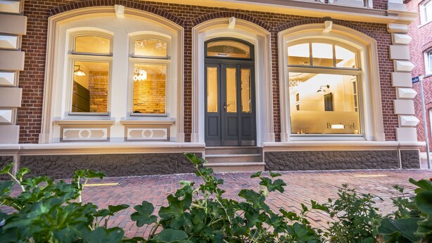 A brick building with a black front door, large arched windows, and a stone foundation. - Burghotel Lingen (Lingen)