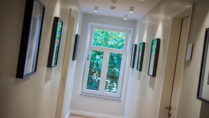 A hallway with framed pictures on the walls, a large window at the end, and a door on the right. - Burghotel Lingen (Lingen)