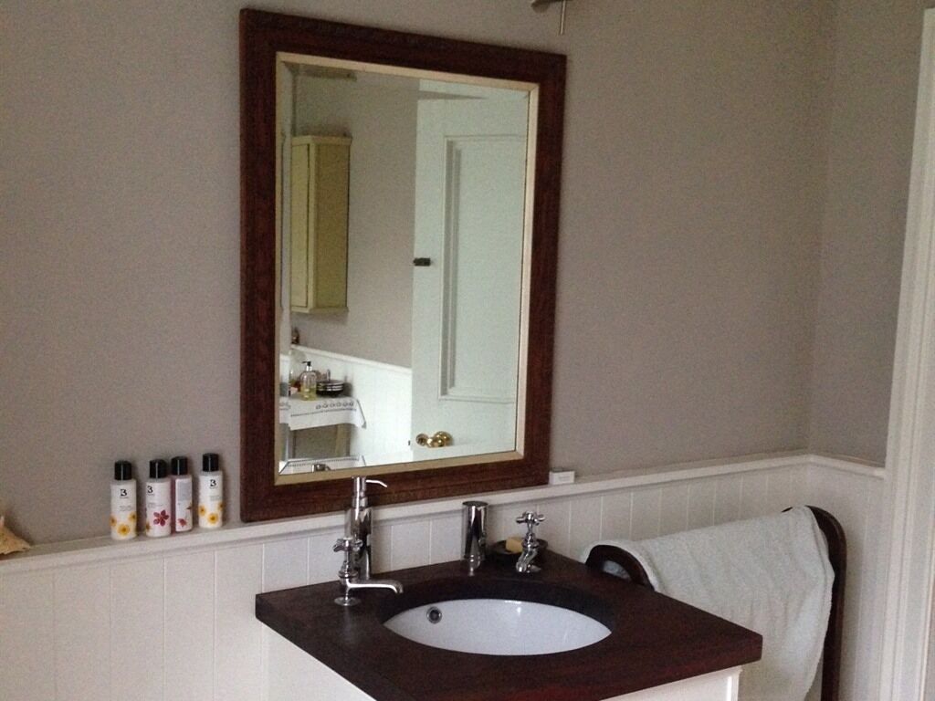A bathroom with a large mirror, a sink with two faucets, and toiletries on the countertop.