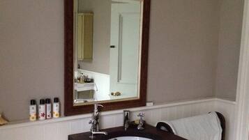 A bathroom with a large mirror, a sink with two faucets, and toiletries on the countertop.