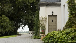 A gravel path leading to a building with a door and a lantern. There is a chair and a potted plant near the door. - Lough Bawn House (Collinstown)