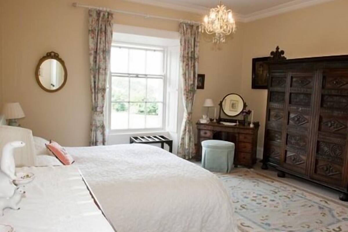A bedroom with a bed, a dresser, a mirror, and a chandelier.