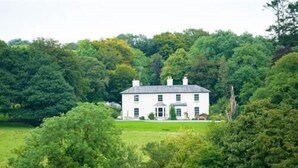 A white house with a symmetrical facade, surrounded by lush greenery and trees. - Lough Bawn House (Collinstown)