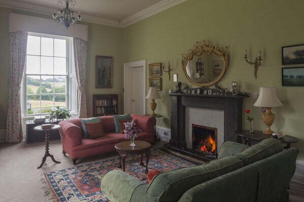 Una sala de estar con chimenea, dos sofás, una mesa de centro y un ventanal con cortinas.