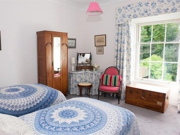 A bedroom with two beds, a wooden wardrobe, a small table, a chair, and a window with a view of greenery. - Lough Bawn House (Collinstown)