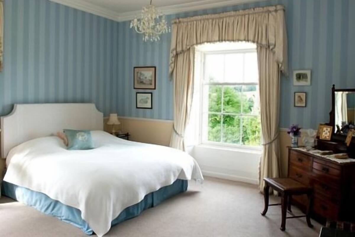 A bedroom with a large bed, a dresser, a mirror, and a window with curtains.