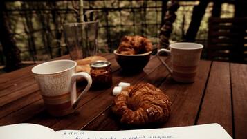 Ein Holztisch mit einer Kaffeetasse, einem Croissant, einer Marmeladenglas und einer Schüssel Kekse.