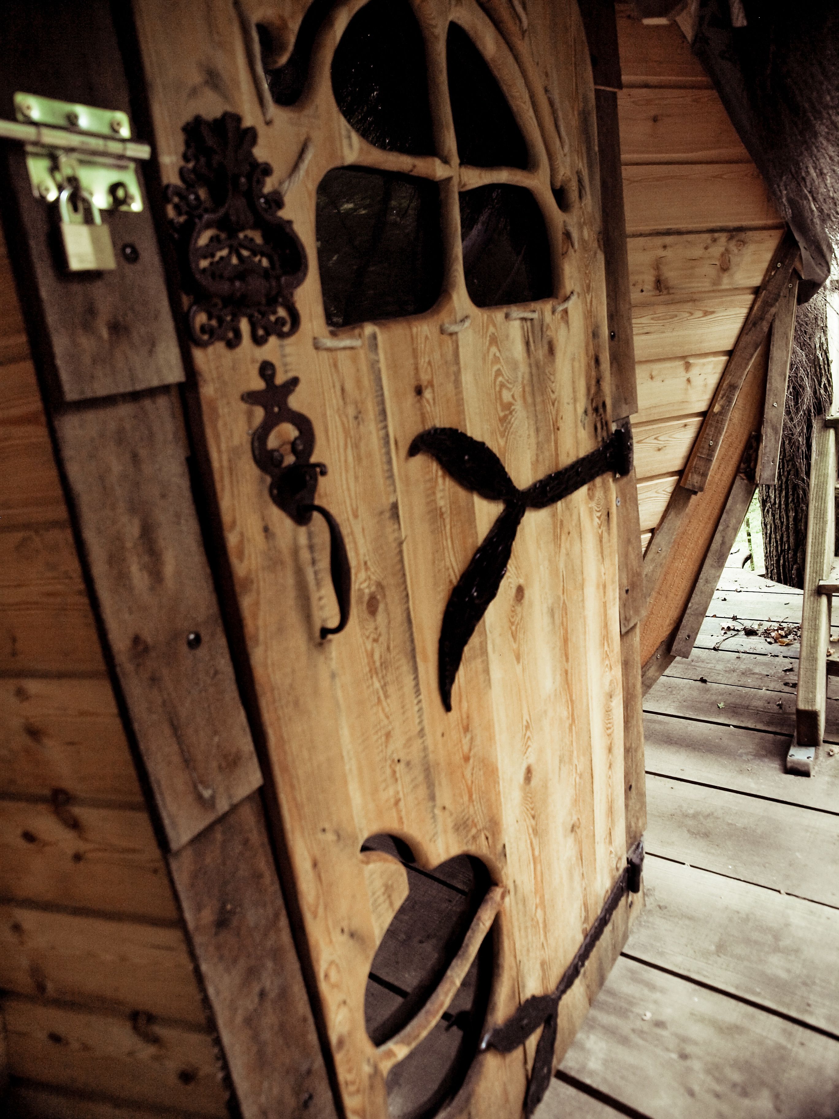 A wooden door with a rustic design, featuring a metal latch and decorative elements.