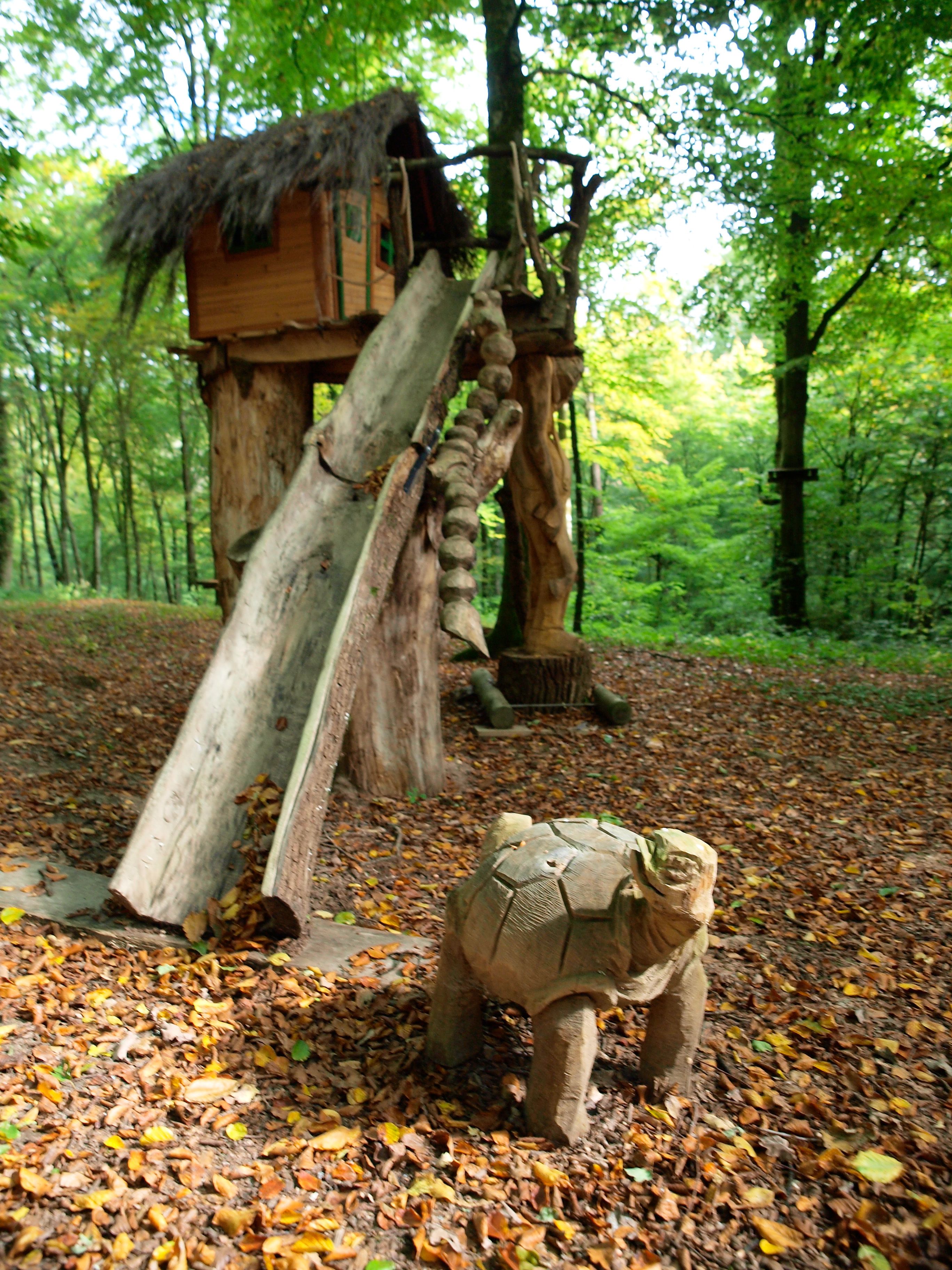 Una estructura rústica de madera con techo de paja, rodeada por un bosque con hojas caídas en el suelo.