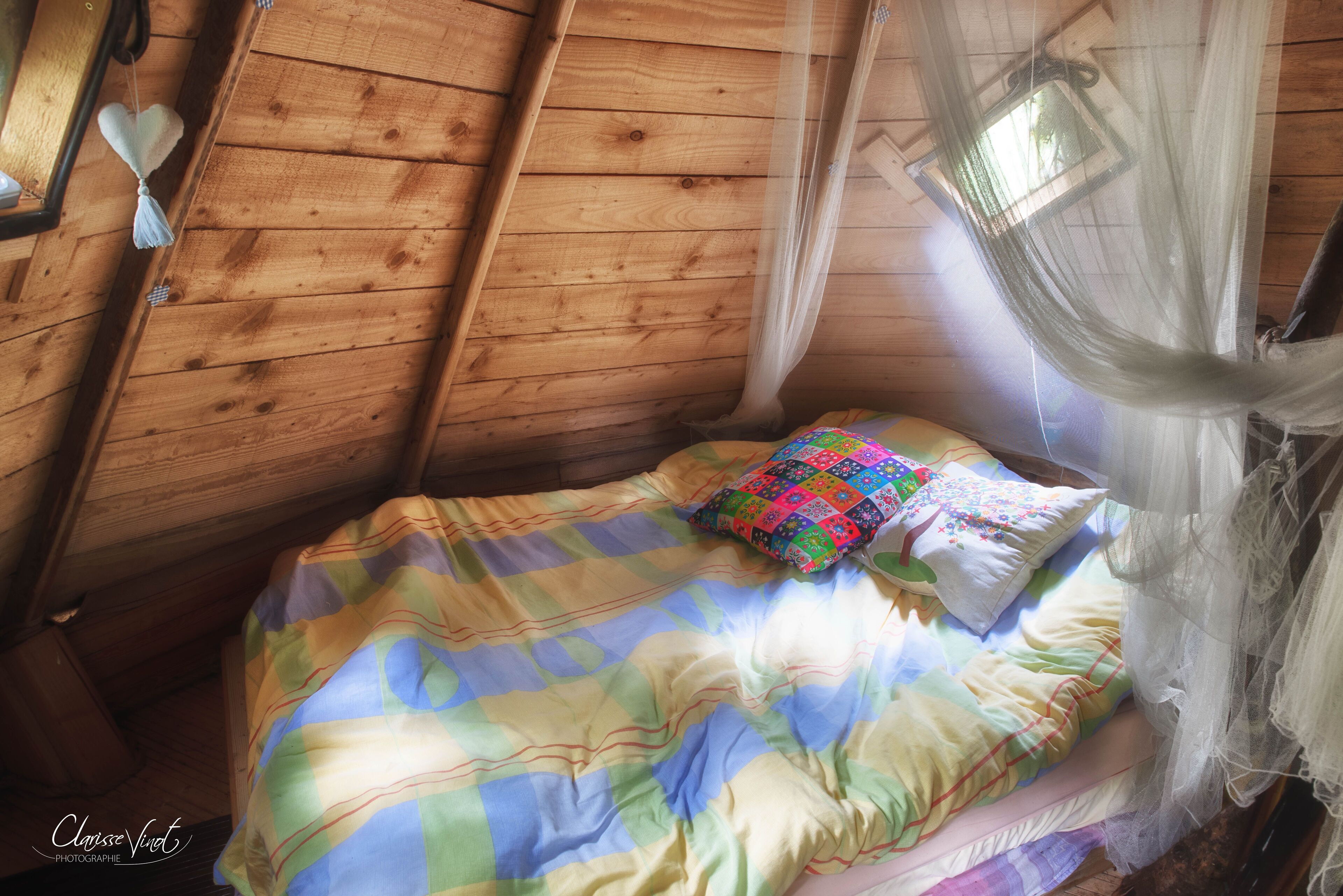 Ein gemütliches Zimmer mit Holzbalkendecke, einem Bett mit bunter Steppdecke, einem Zierkissen und einem Moskitonetz.