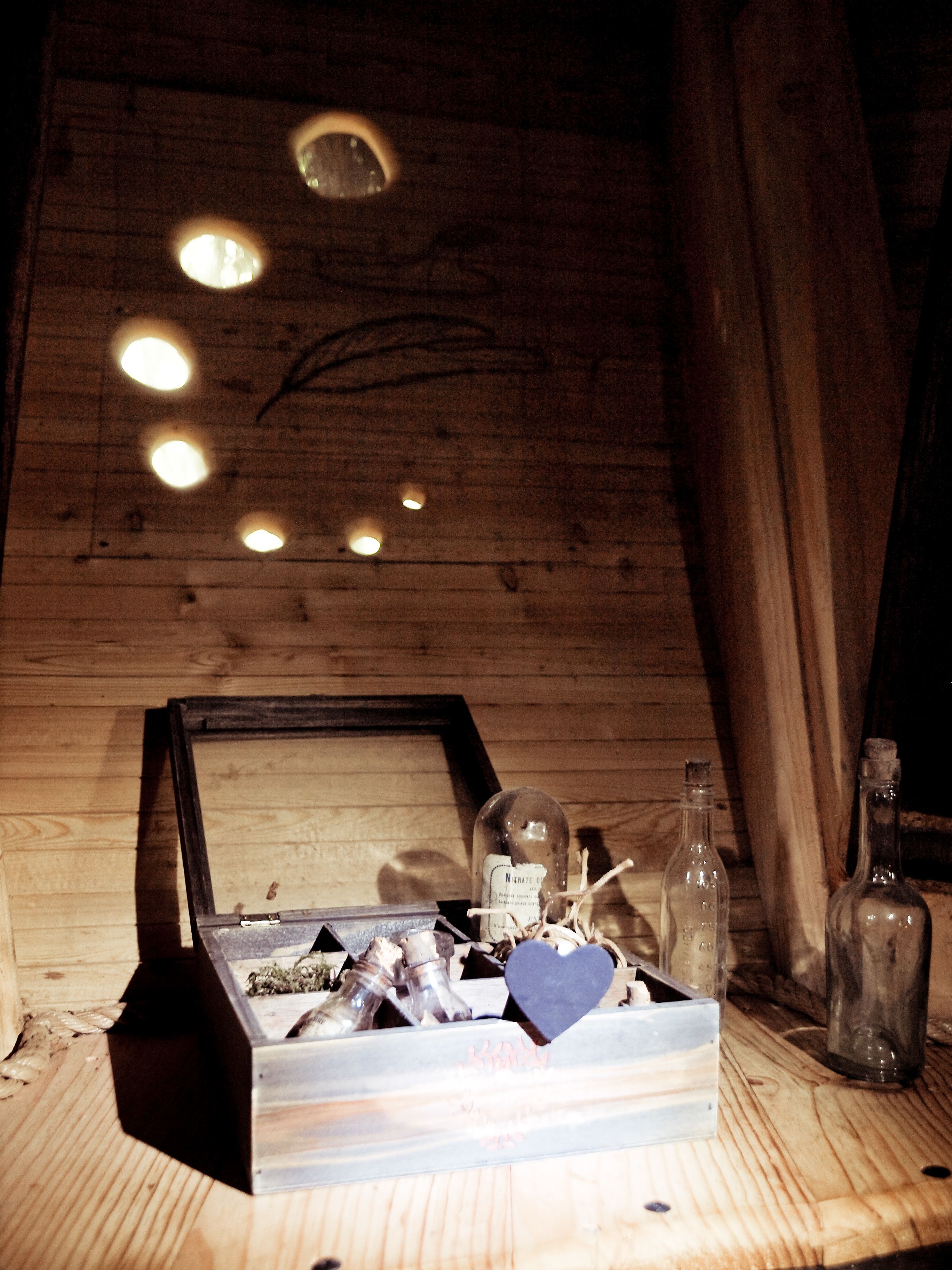 Ein Schlafzimmer im Dachgeschoss mit Holzbalken, schrägem Dach, einem gerahmten Bild und einem Holztisch mit Flaschen und einer Kiste.