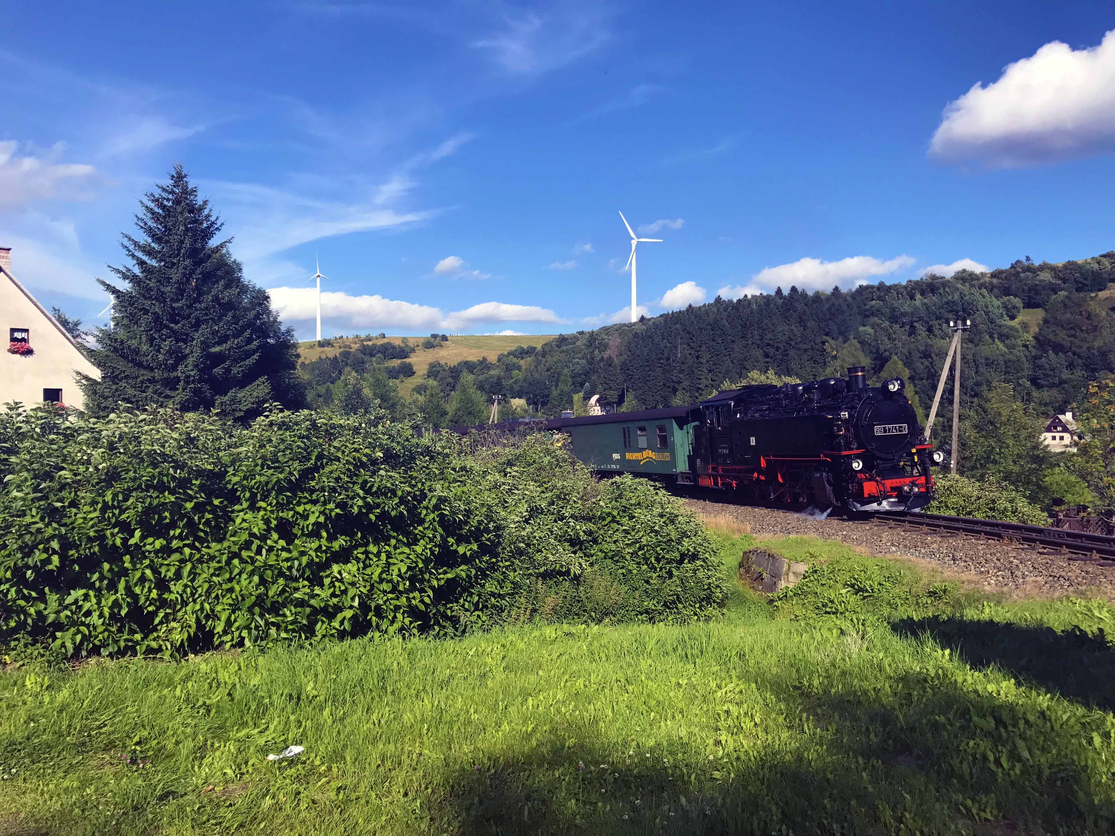 A steam locomotive on a railway track with wind turbines in the background.