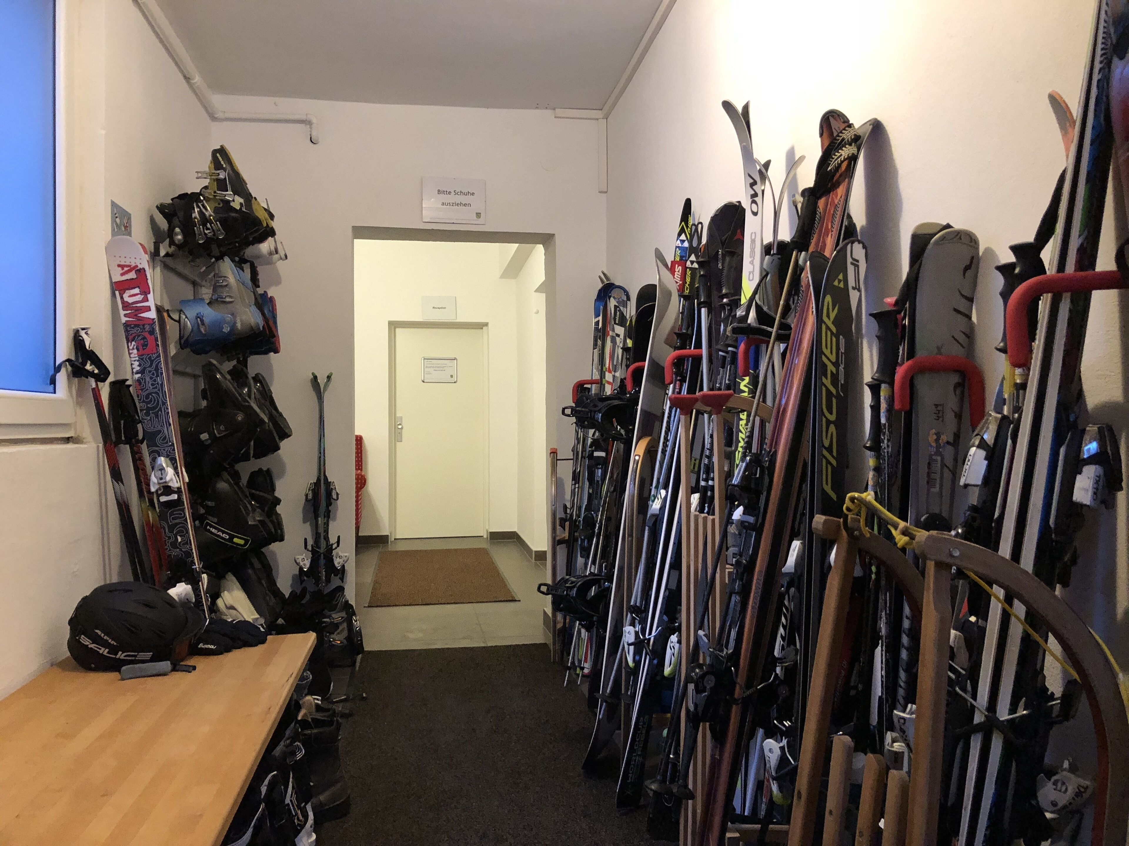 Una stanza per il deposito sci con sci e snowboard su rastrelli, una panca in legno e una porta all'estremità.