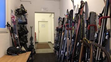 Una stanza per il deposito sci con sci e snowboard su rastrelli, una panca in legno e una porta all'estremità.