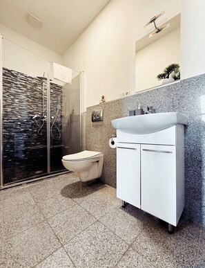 Un baño moderno con cabina de ducha de vidrio, un inodoro blanco y un lavamanos con encimera de granito.