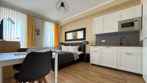 A modern hotel room with a bed, bedside table, lamp, and a kitchenette with a microwave. - Apartments Fichtelberger Blick (Oberwiesenthal)