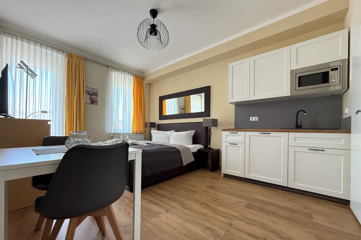Una habitación de hotel moderna con cama, mesita de noche, lámpara y una kitchenette con microondas.
