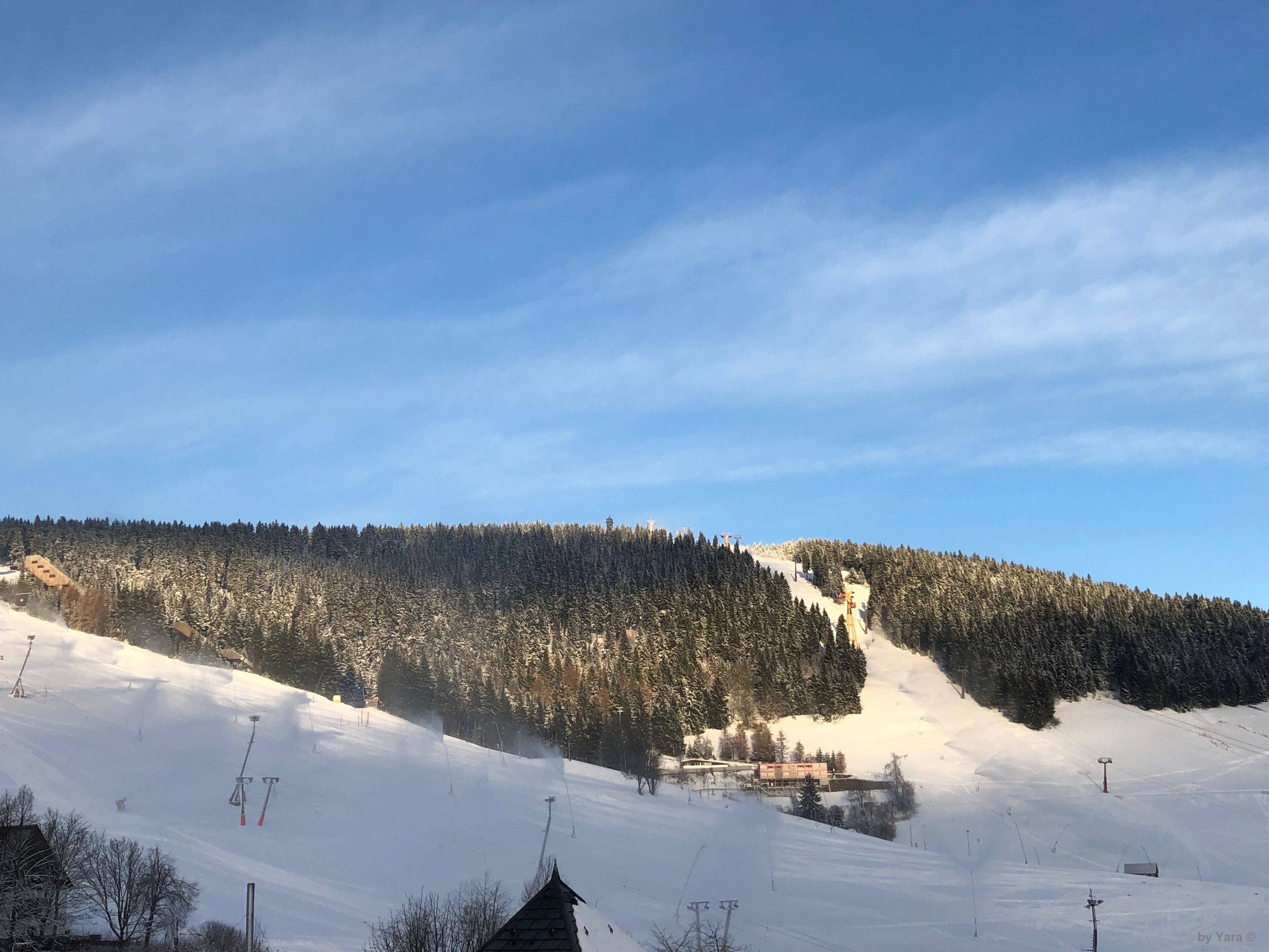 A snowy ski slope with a ski lift and a building in the background.