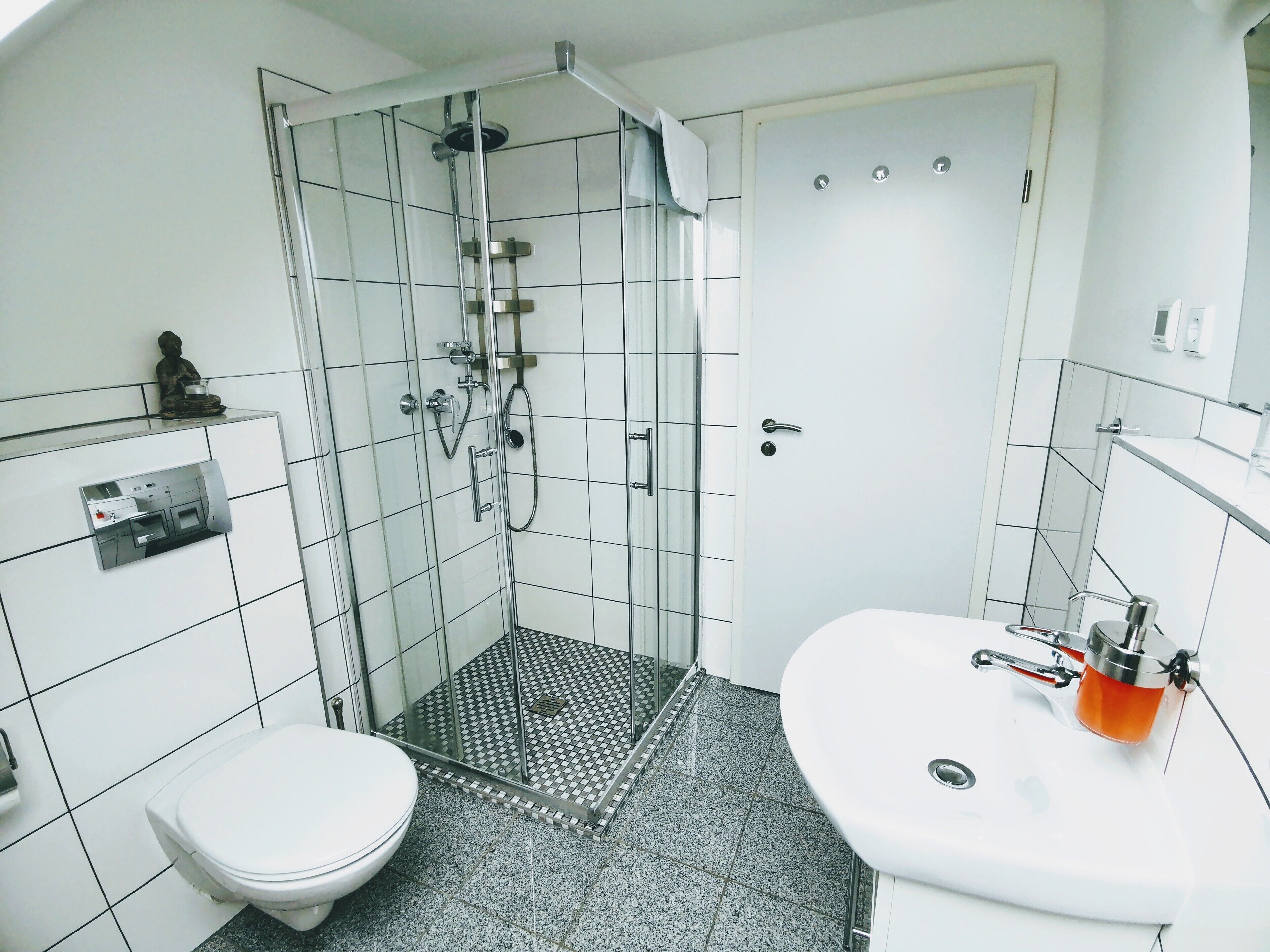 Une salle de bain moderne avec une douche à parois de verre, des toilettes blanches et un lavabo doté d’un distributeur de savon orange.