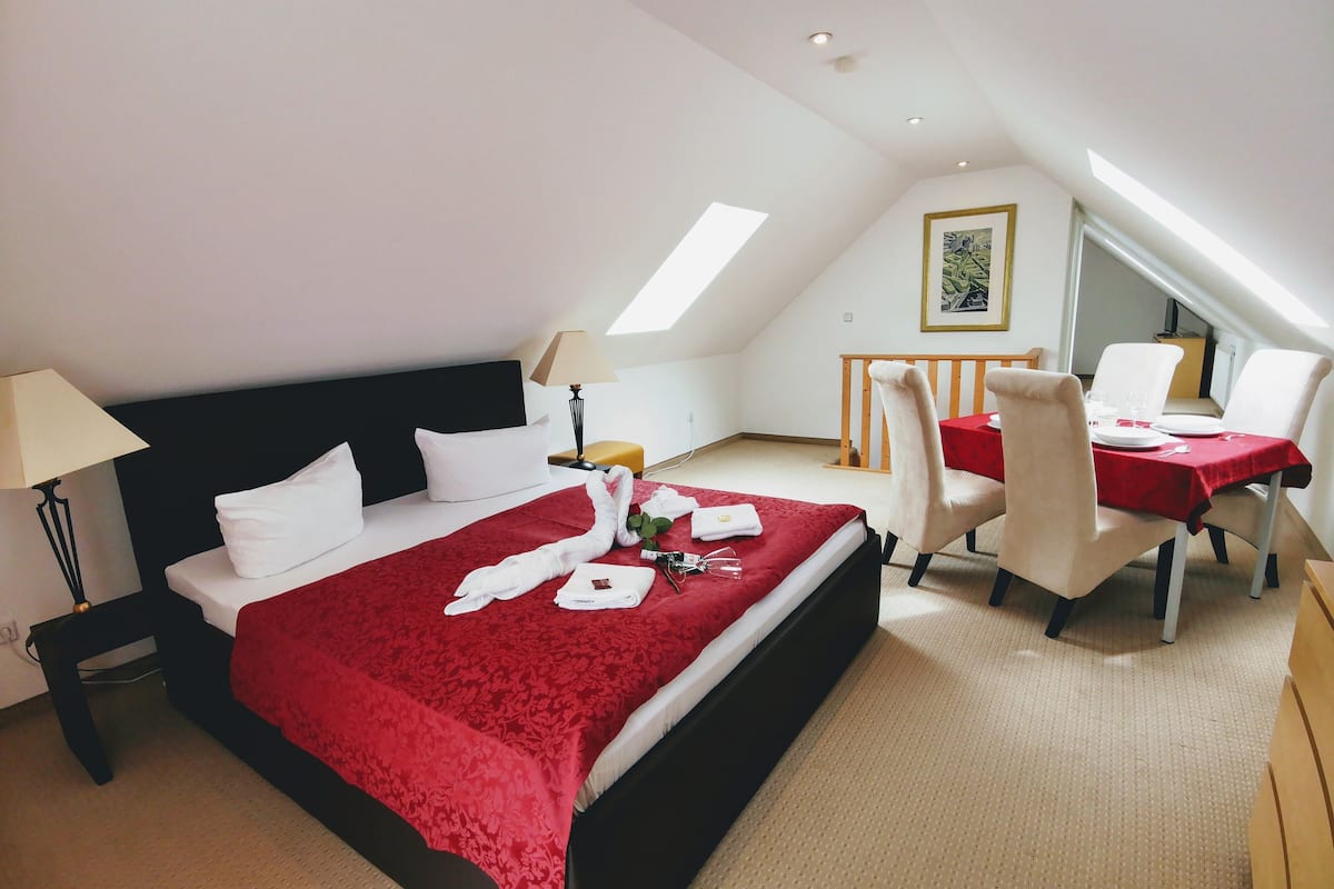 Habitación de hotel con cama, una mesa de comedor con sillas, una lámpara y un cuadro en la pared.