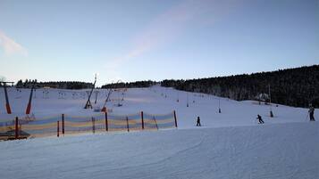 A snowy ski slope with a fence, ski lift, and trees in the background.