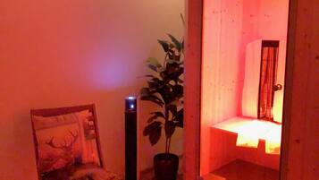 Una habitación con suelo de madera, una silla con un cojín estampado con un ciervo, una planta en maceta y una mesita de noche con una lámpara.