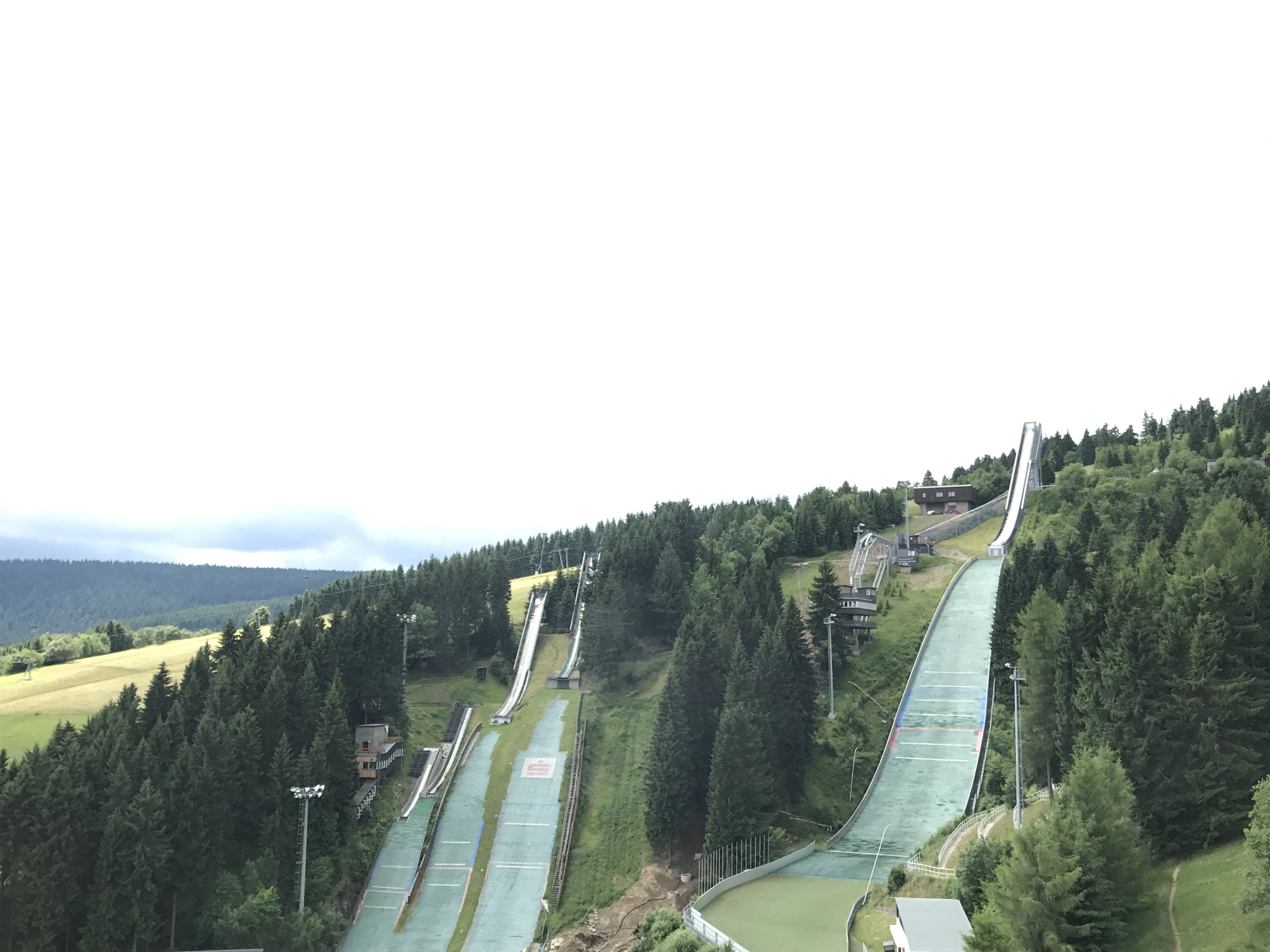 A ski slope with multiple runs, surrounded by dense forest and a distant mountain range.