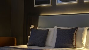 Una cama bien tendida con una colcha a rayas y almohadas, un cabecero y cuadros enmarcados en la pared.