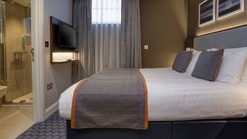 Una habitación de hotel moderna con una cama grande, un televisor montado en la pared, una zona de ducha y vistas a la ciudad.