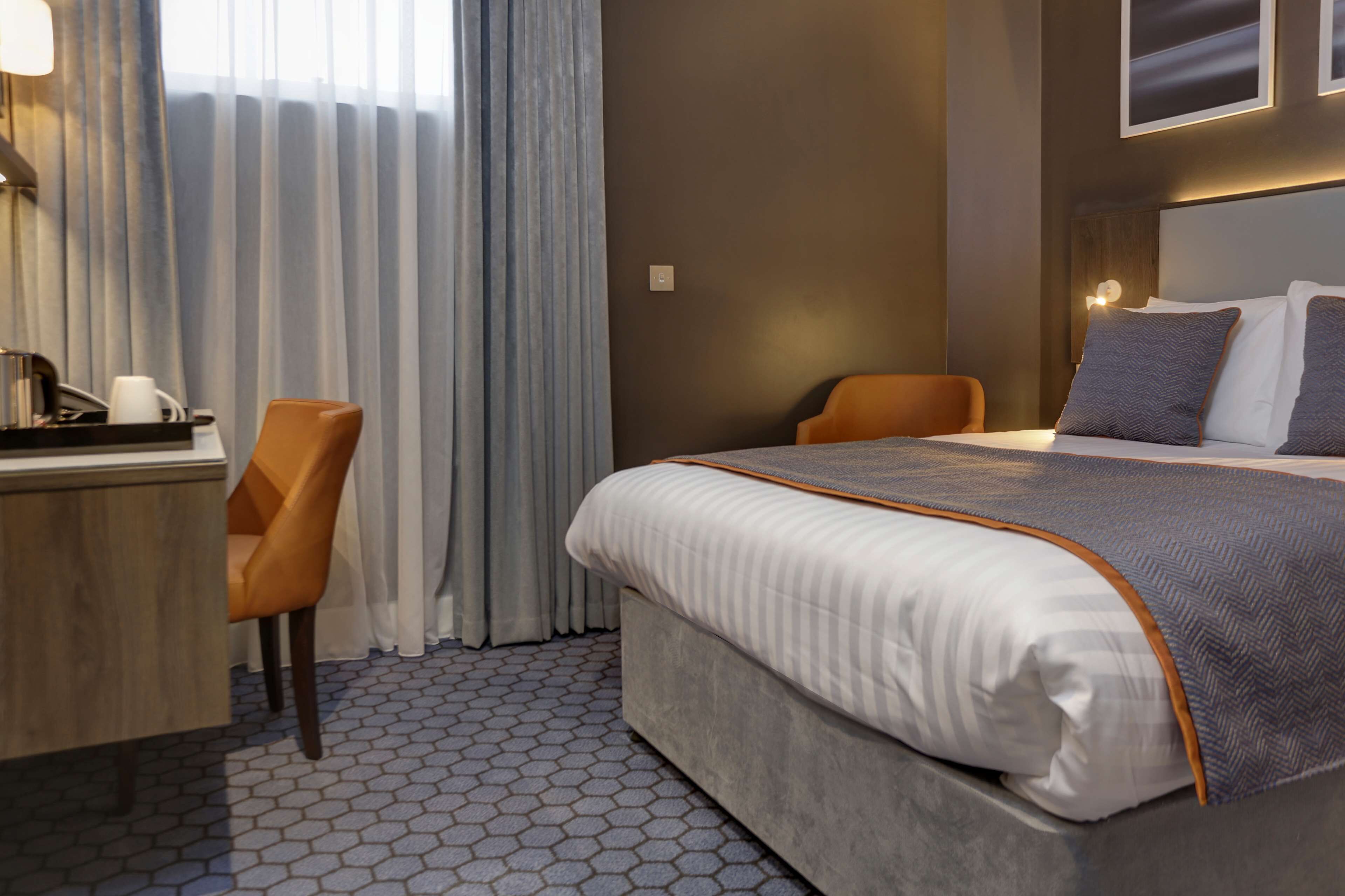 A hotel room with a large bed, a desk with a chair, and a view of the outside through curtains.