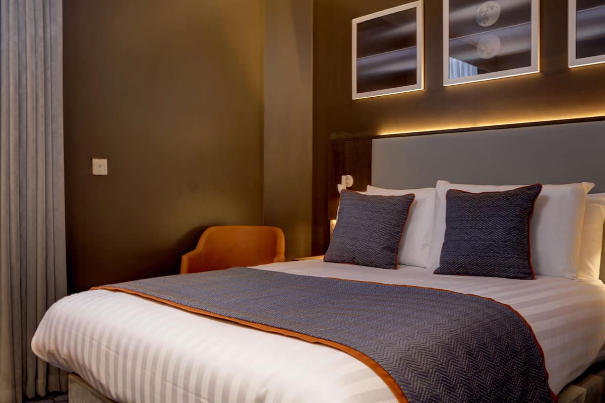 Une chambre d’hôtel avec un grand lit, une chaise et trois tableaux encadrés accrochés au mur.