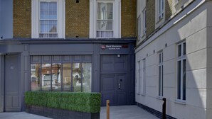 Un edificio con una puerta gris grande y ventanas, un cartel que dice "Best Western PLUS Vauxhall Hotel", y un pequeño seto verde al frente.