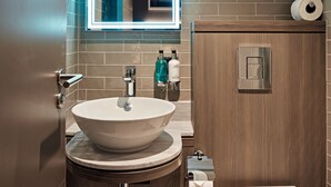 Un baño moderno con un lavabo redondo, un espejo con luz de neón, un mueble de madera y un inodoro.