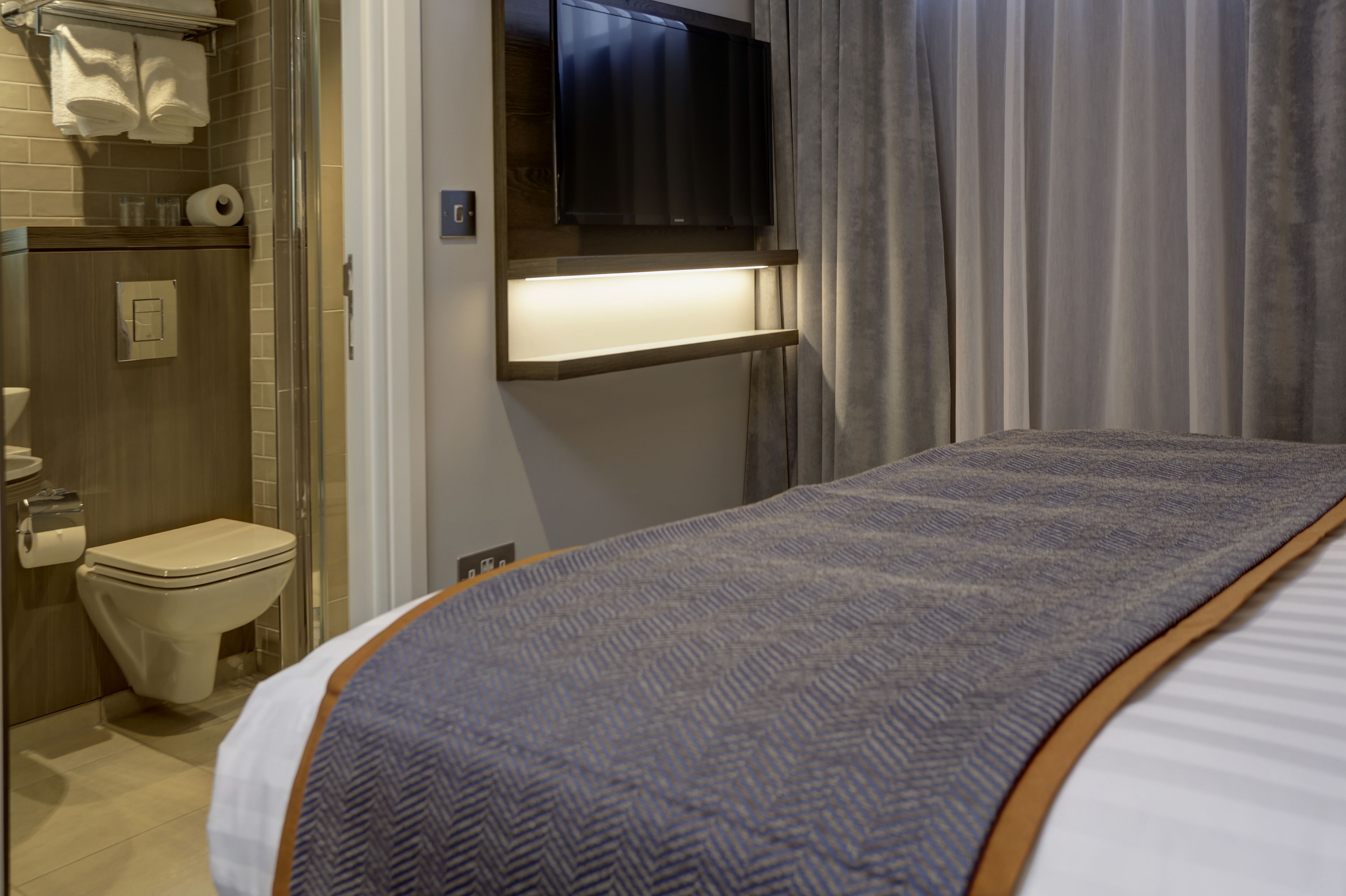 A hotel room with a bed, a TV mounted above the bed, a shower area, and a toilet.