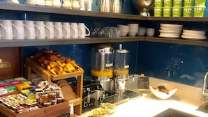 Una barra de desayuno con una variedad de alimentos, máquinas de café y un frutero.