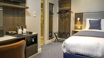 Ein Hotelzimmer mit Bett, Schreibtisch mit Telefon, Stuhl, Kleiderhaken und einem kleinen Tisch.