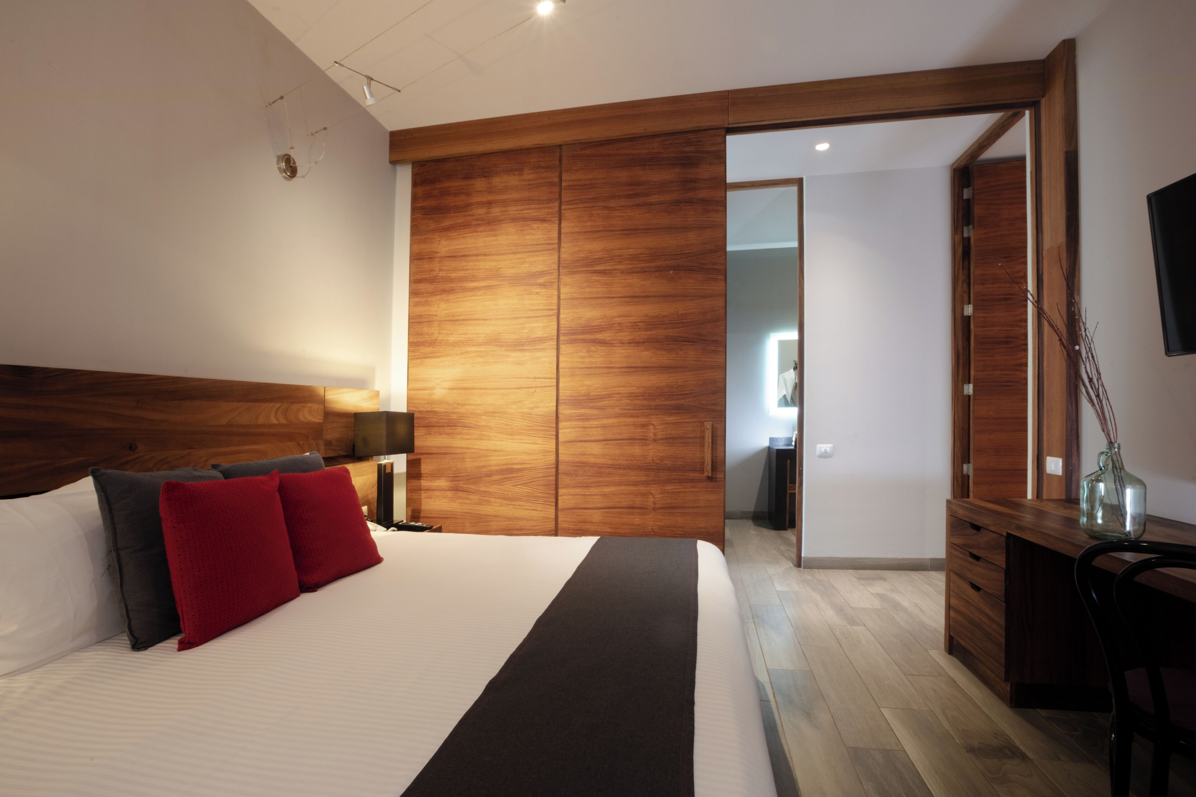 Un dormitorio moderno con una cama grande, armario de madera, escritorio y televisor montado en la pared.