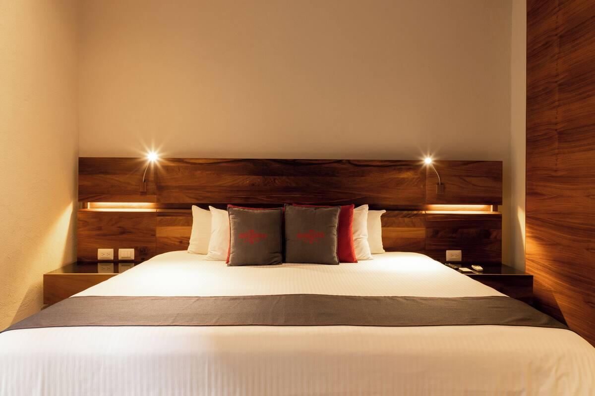A neatly made bed with a headboard, bedside tables, and wall-mounted lighting.