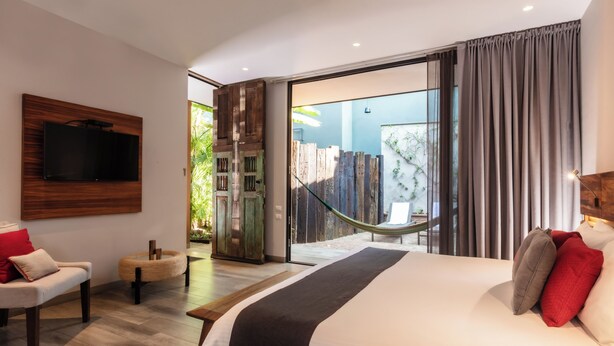 Un dormitorio moderno con una cama grande, un televisor montado en la pared, una hamaca y un ventanal corredizo que da a un espacio exterior.