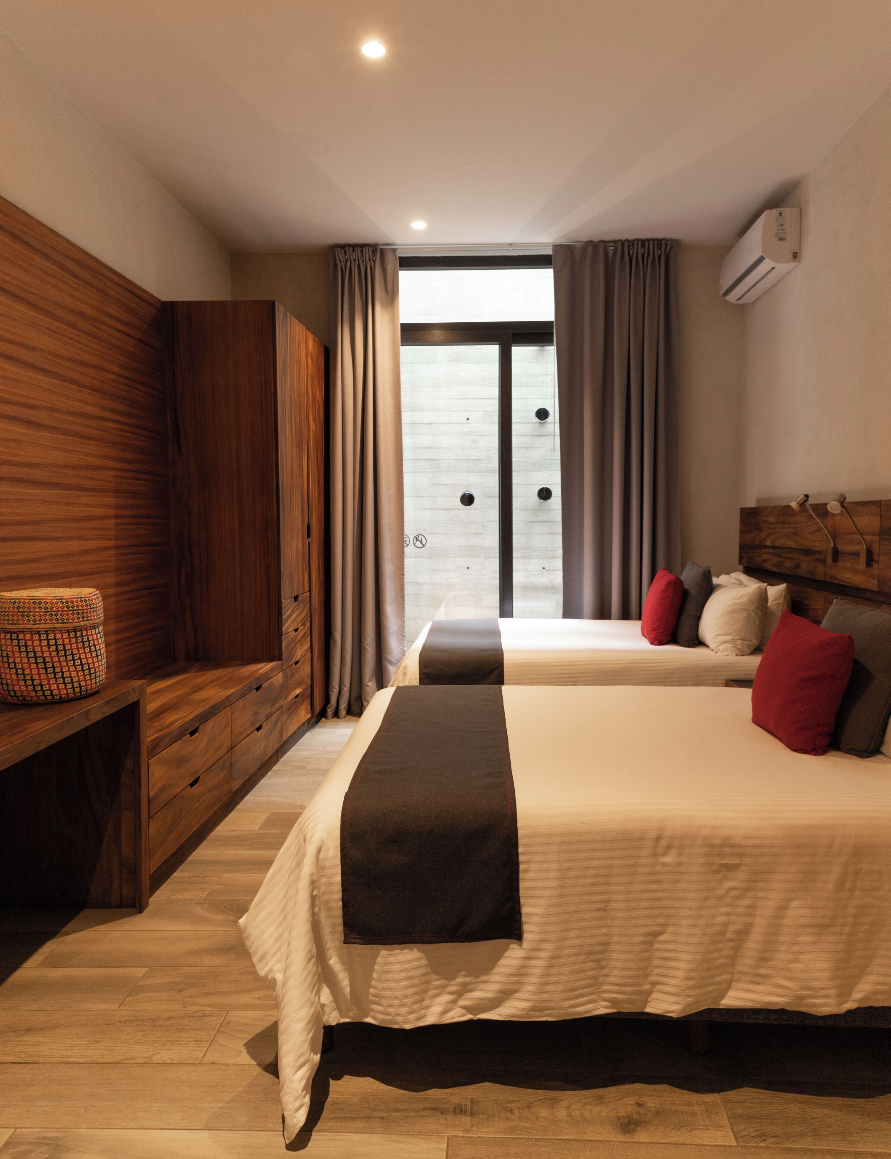 Una habitación de hotel moderna con dos camas, un armario de madera, un escritorio y un ventanal con cortinas.