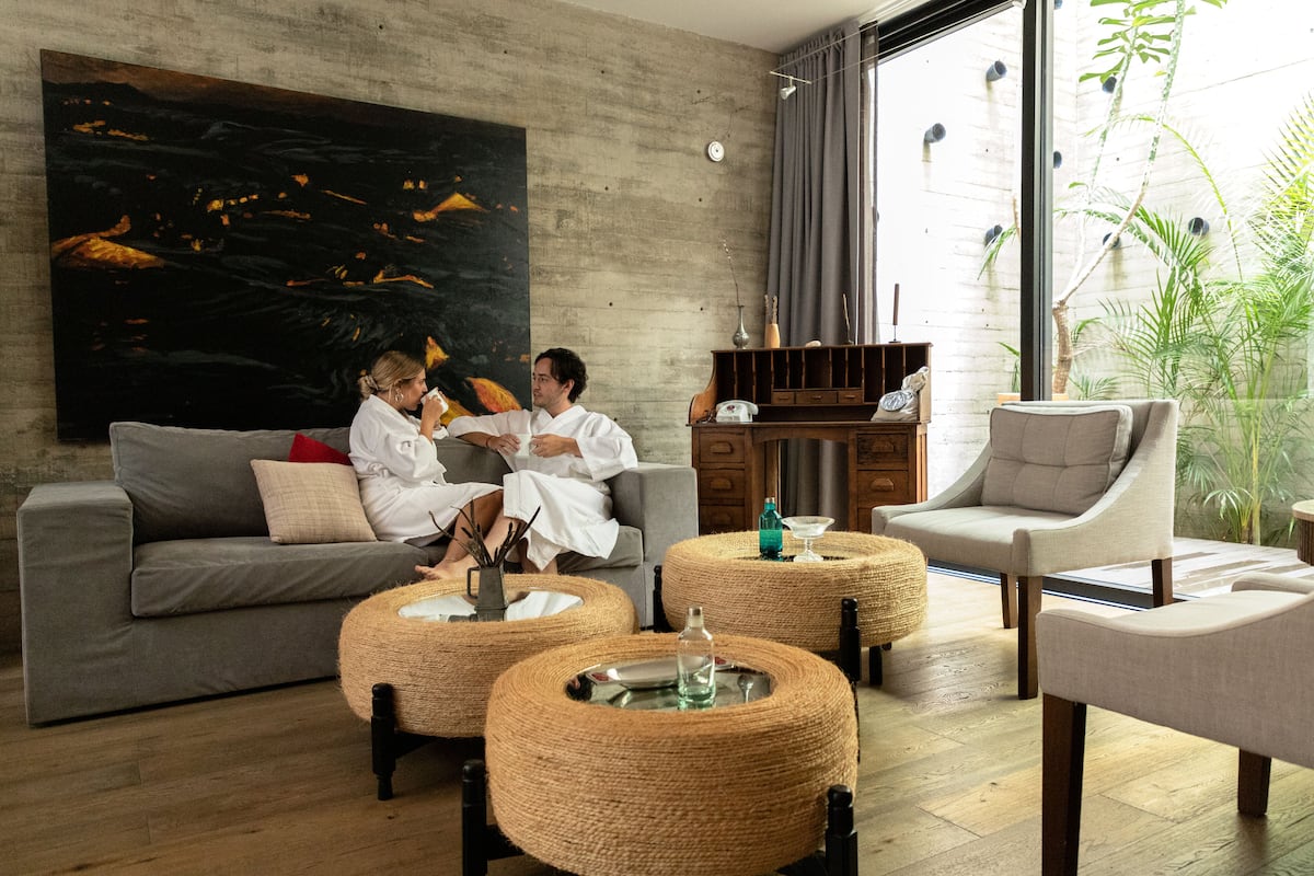 A modern living room with a grey sofa, two round wicker ottomans, a white armchair, and a large abstract painting on the wall.