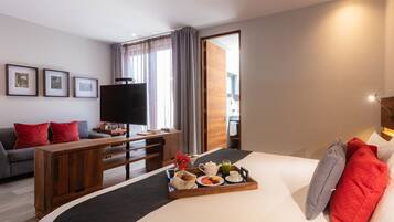 Habitación de hotel con cama, escritorio, sofá y televisor. Hay una bandeja con alimentos para el desayuno sobre la cama.