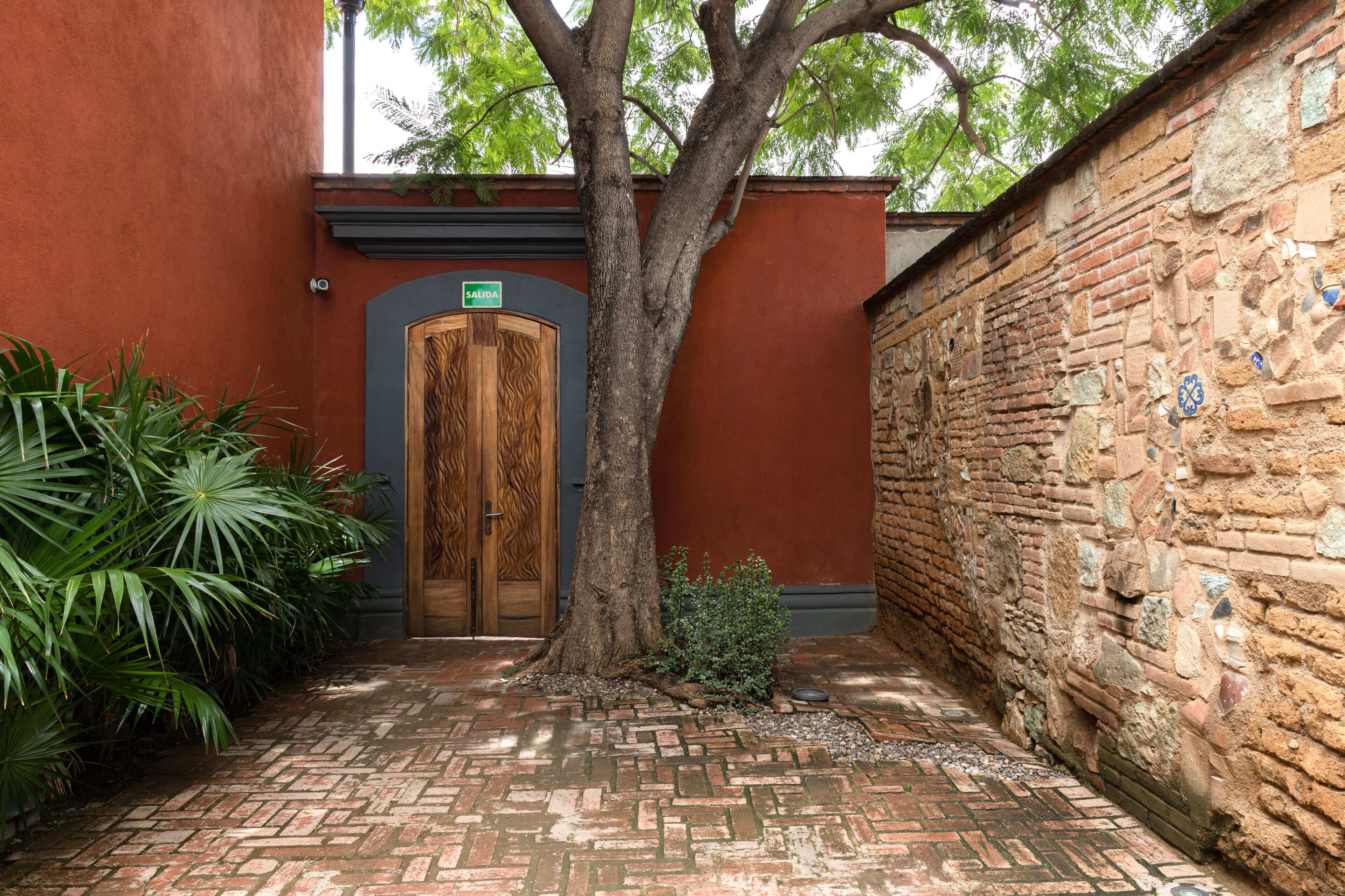 Un patio con puerta de madera, un árbol y un muro de ladrillo con mosaicos.