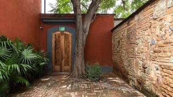 Un patio con puerta de madera, un árbol y un muro de ladrillo con mosaicos.