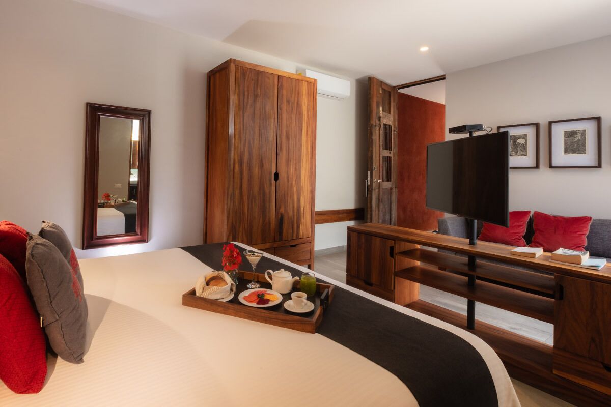 A hotel room with a large bed, wooden wardrobe, a desk with a television, and a tray with breakfast items.
