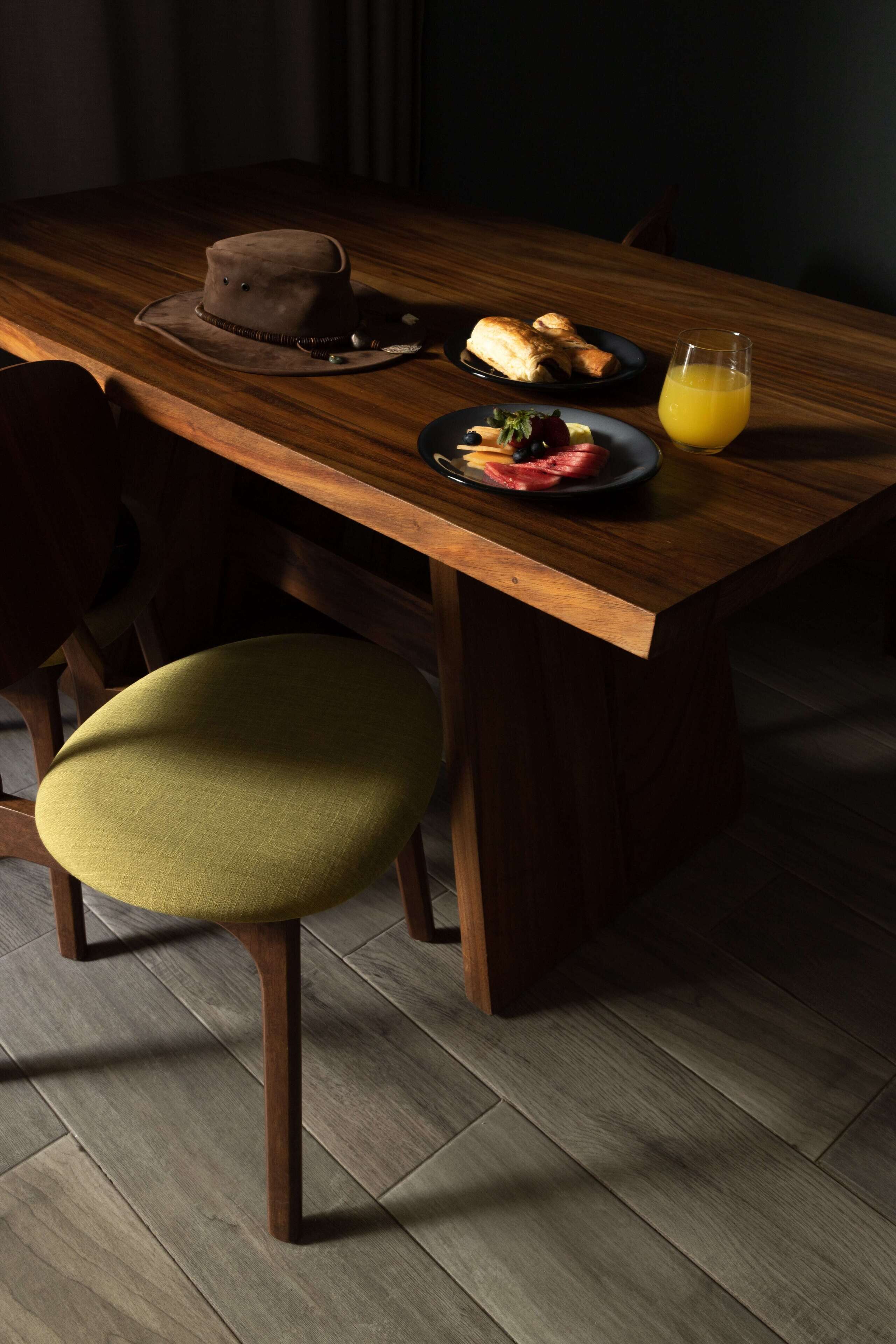 Una mesa de madera con un sombrero, croissants, fruta y un vaso de jugo de naranja.