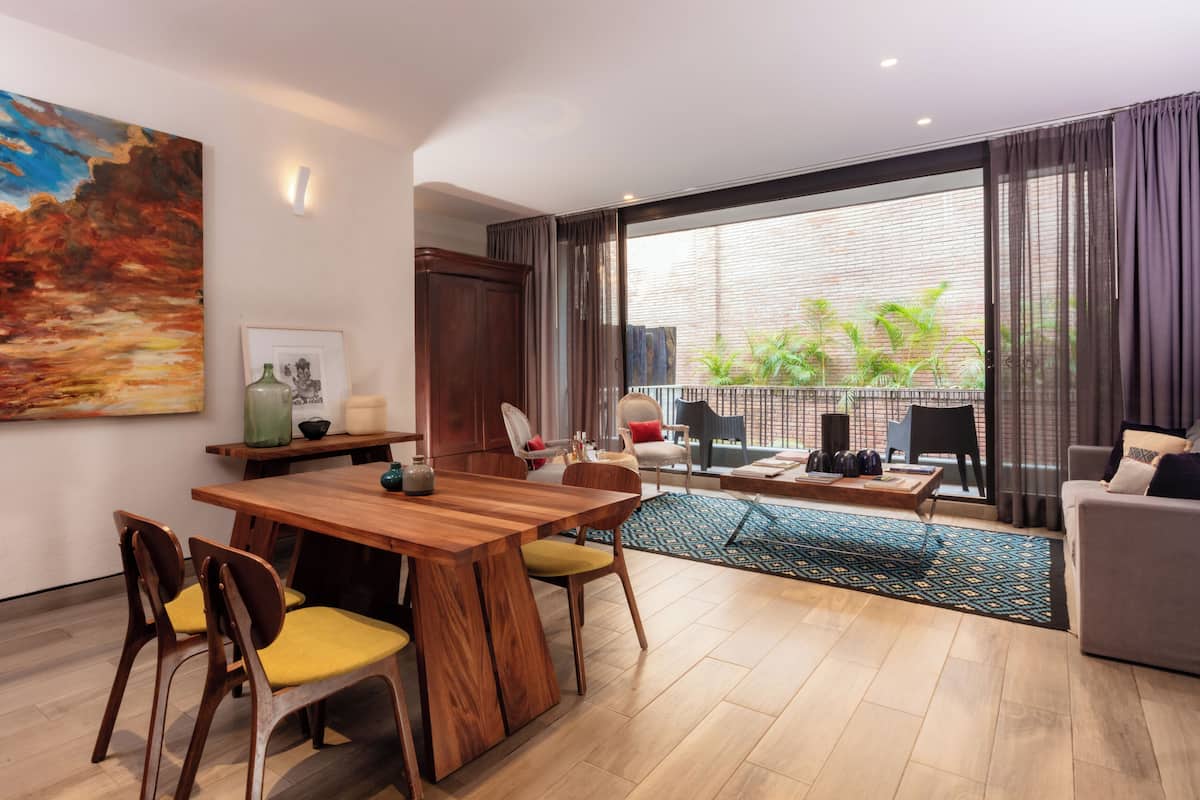 A modern living room with a wooden dining table, yellow chairs, a grey sofa, and a balcony with plants.